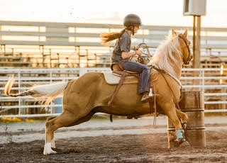 Rylen barrel racing in the arena at sunset